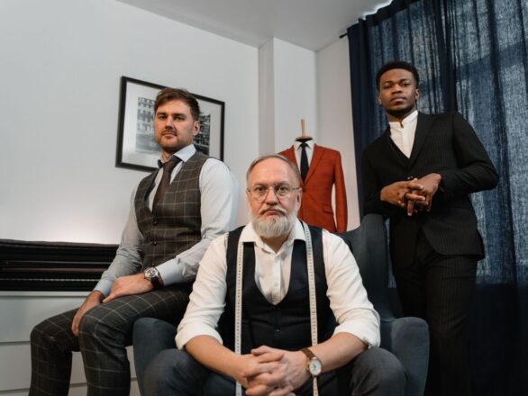Drie mannen in maatpakken in een atelier met stoffen en een paspop