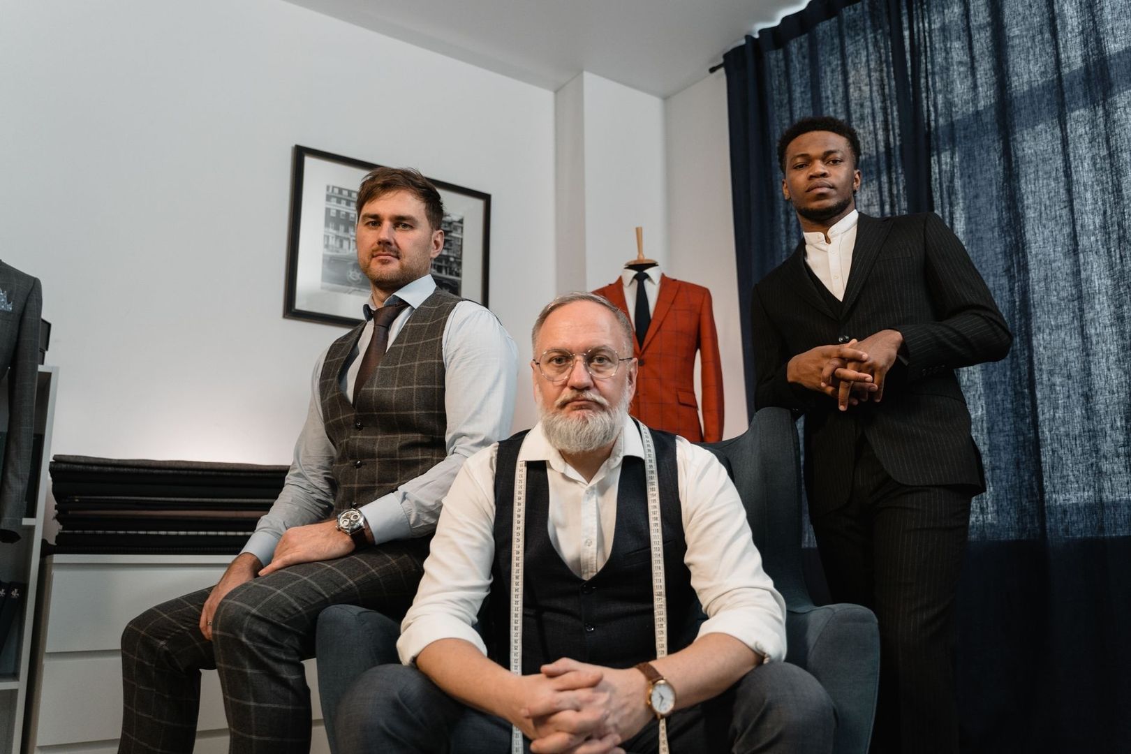 Drie mannen in maatpakken in een atelier met stoffen en een paspop